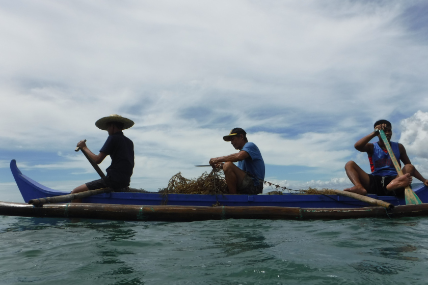 Photo à contre jour : une barque sur l'eau avec 3 pêcheurs