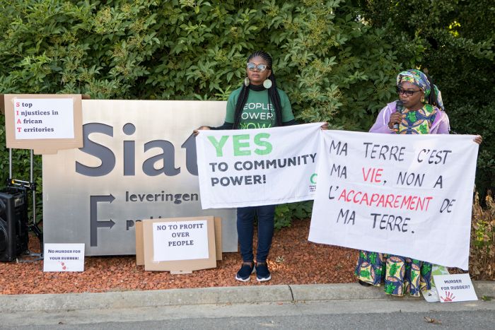 Deux manifestantes d'origine africaines devant l'enseigne de société SIAT, avec des pencartes "Ma terre c'est ma vie, non à l'accaparement de ma terre." et "Yes to community power"