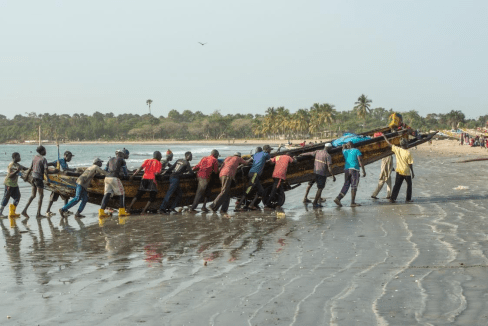 Une vingtaine de pecheurs africains à la plage, en train de sortir un bateau de l'eau