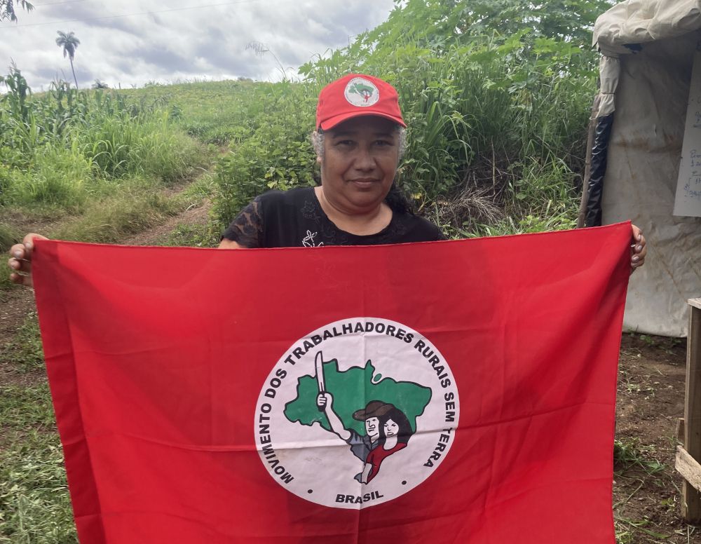 Photo d'une femme face caméra qui tien un drapeau rouge avec l'emblème du Movimento dos trabalhadores rurais sem terra - Brasil