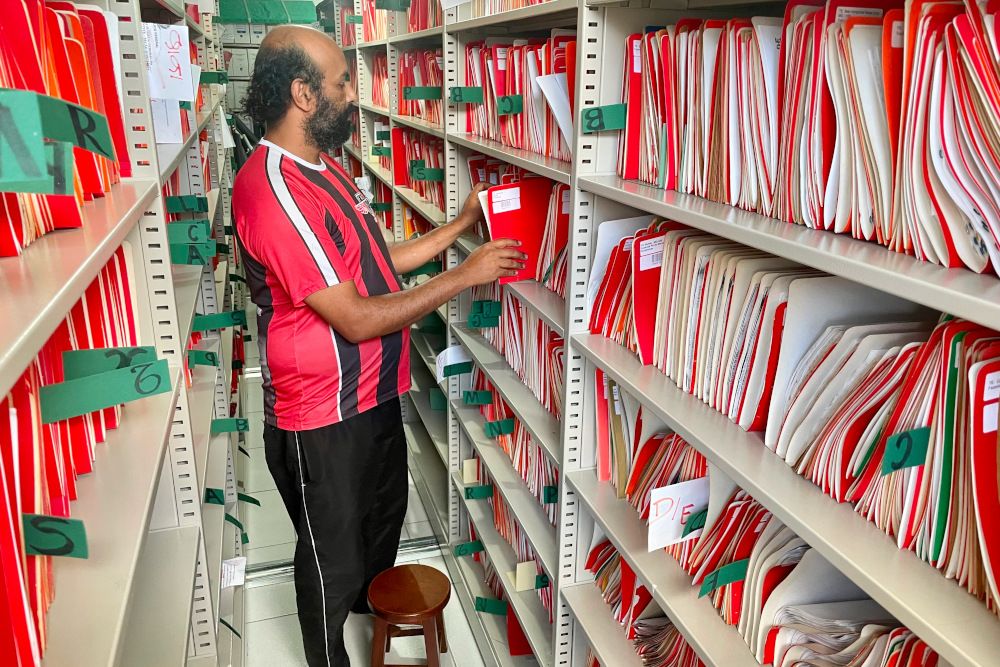 un homme entre des étagères d'un archive remplie de classeurs rouges