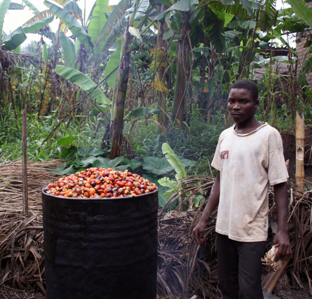 Un paysan africain à coté d'un bidon métallique remplie des fèves rouges