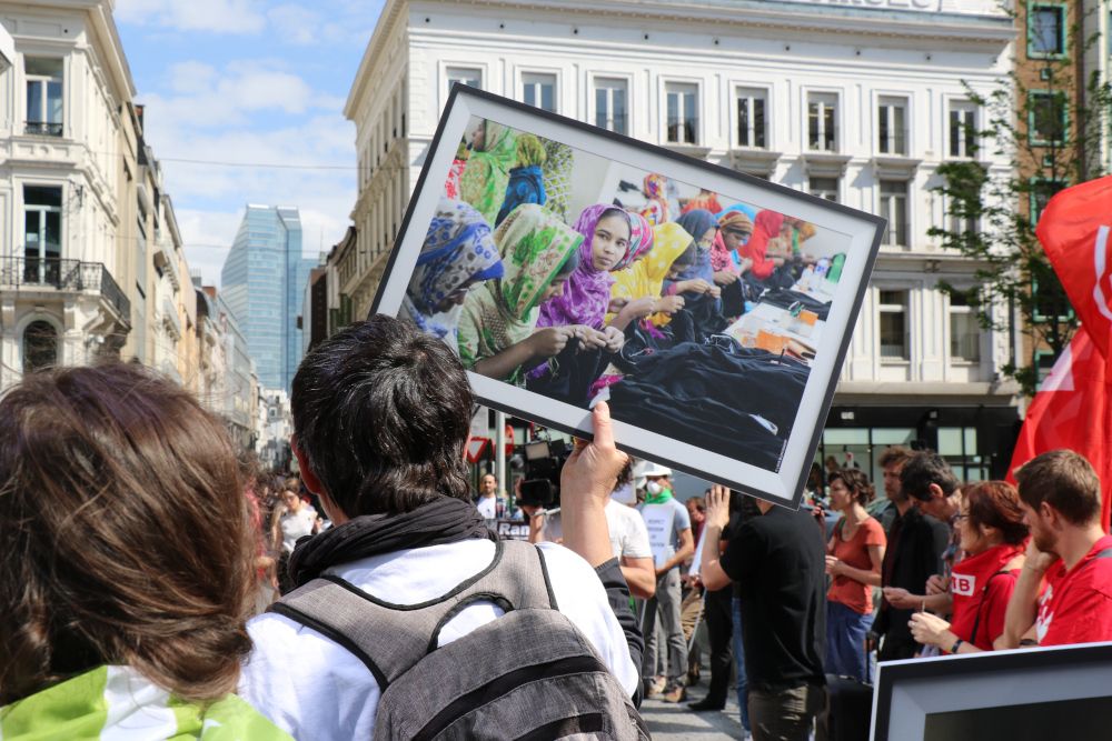 des manifestants debout en cercle, une personne tient une photo de travailleuse de textile asiatiques