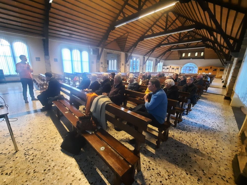 L'intérieur d'une église, une 30aine de personnes assise dans les bancs. Devant Christophe Cornet debout parlant dans un micro.