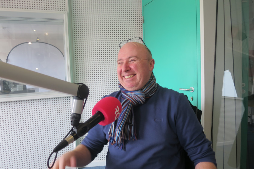 Dans un studio radio un homme riant devant un microphone.