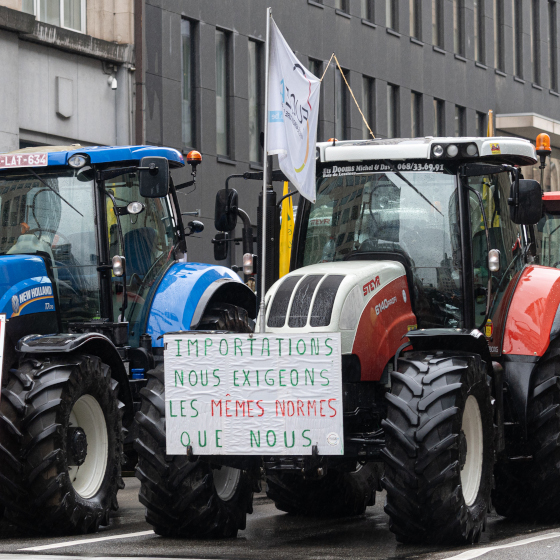 Deux tracteurs devant des bâtiments de bureau, un porte une grande pancarte : Importations - nous exigeons les mêmes normes que nous