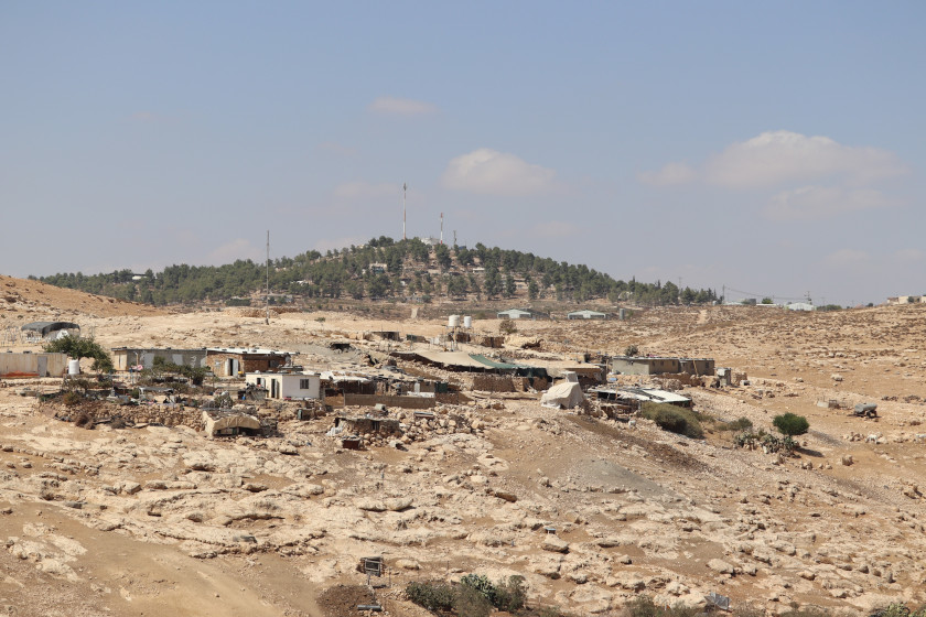 Des maisons isolées dans un paysage aride. En arrière-plan, des antennes émergent d'une forêt.