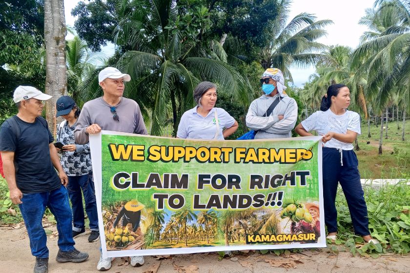 5 Philippins a l'extérieur tenant une affiche "We support farmer claim for right to lands"