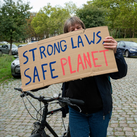 Une personne à coté d'un vélo tient une pancarte avec le texte Strong Laws Safe Planet