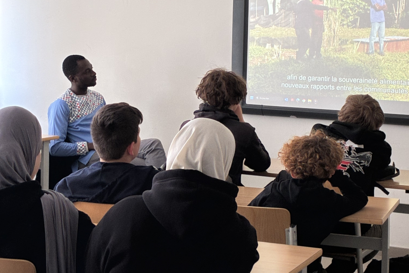 Dans une salle de classe des jeunes ados vue de dos et un adlult regardent une projection