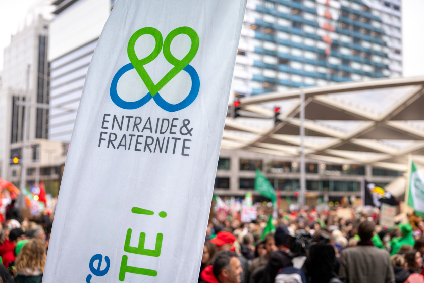 Bannière “Entraide & Fraternité” au premier plan lors d’une manifestation dans une rue urbaine.