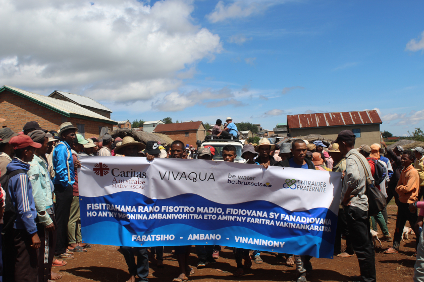 Groupe de personnes marchant dans une rue, tenant une grande banderole de sensibilisation à l’accès à l’eau, à l’hygiène et à la vaccination à Madagascar.